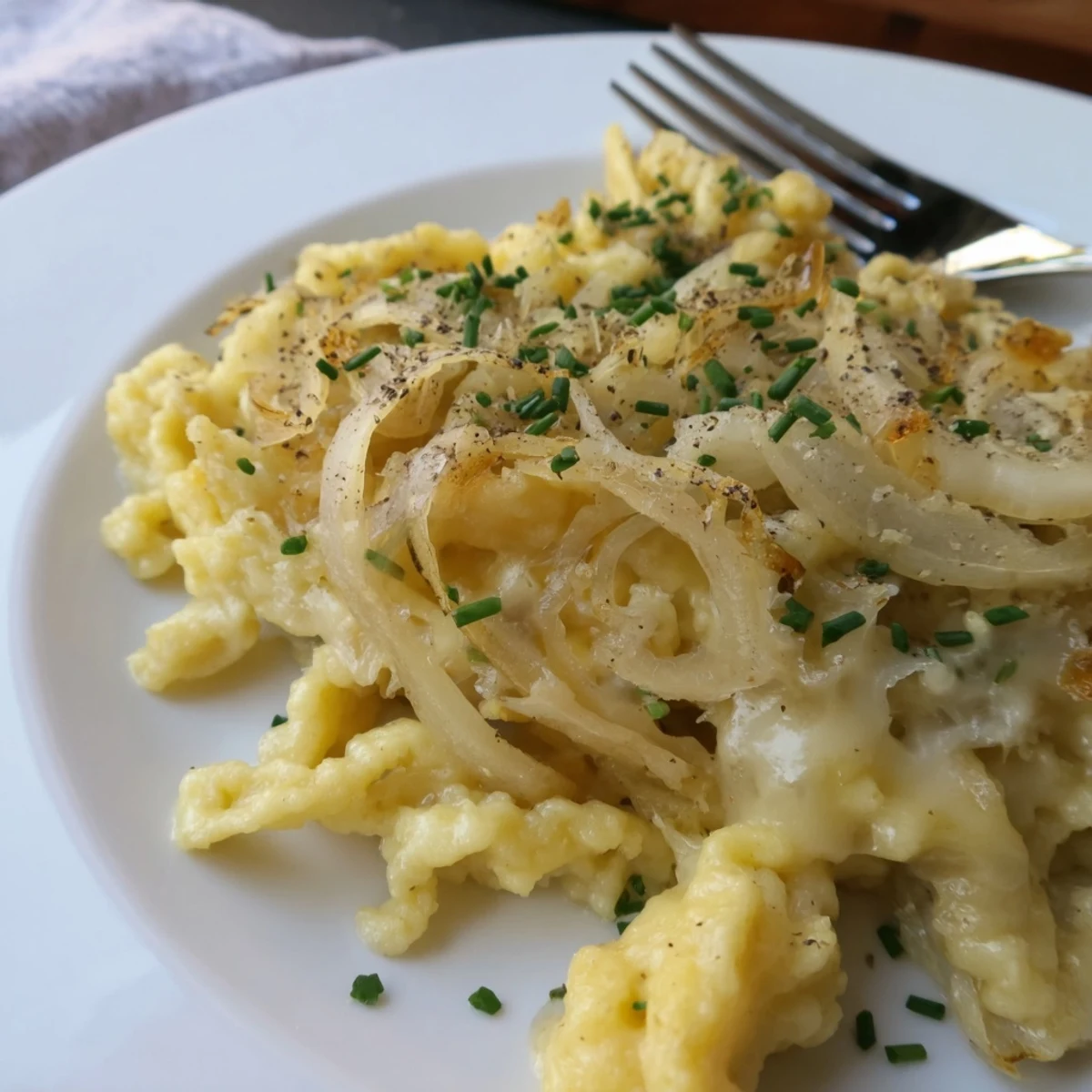 Gebackene Käse-Spätzle mit goldbraunen Zwiebeln, ein herzhaftes deutsches Gericht.  