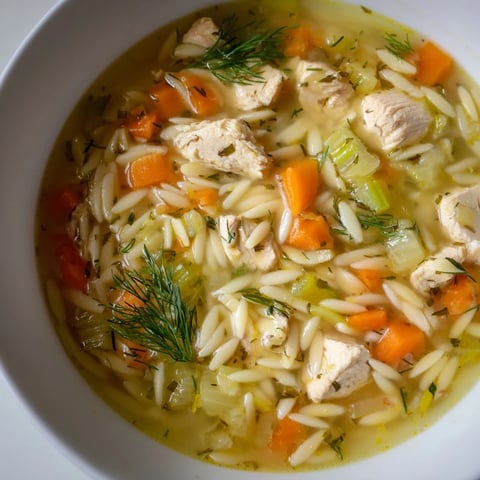 Ein dampfendes Topf mit Chicken Lemon Orzo Soup, gefüllt mit zartem Hühnchen, goldenen Orzo-Nudeln und frischen Kräutern, serviert im rustikalen Keramikschüssel.