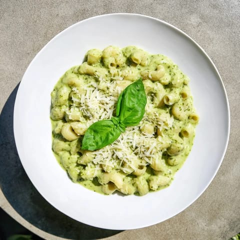 Goldene Nudeln mit cremiger Avocado-Basilikum-Pesto-Sauce, garniert mit frischen Basilikumblättern und geriebenem Parmesan.